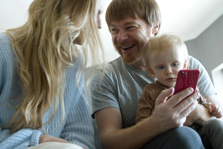 a man and woman sitting on a couch looking at a cell phone, by Eero Järnefelt, pexels, father with child, looks like domhnall gleeson, up close picture, toddler