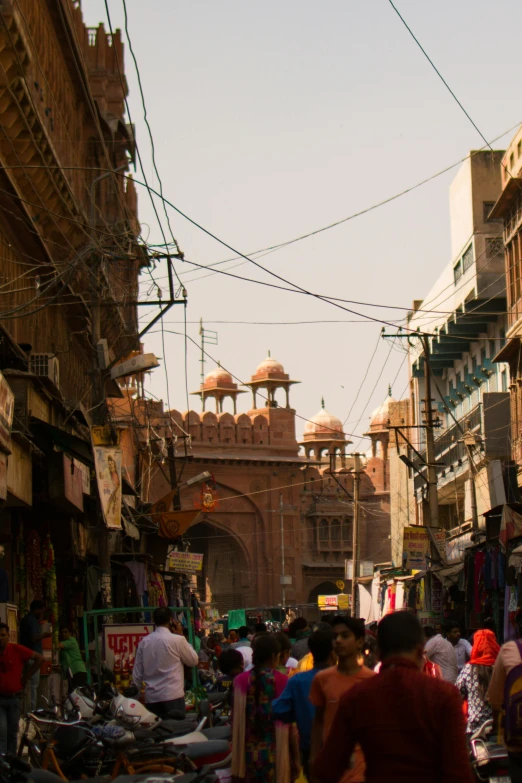 a crowd of people walking down a street next to tall buildings, a picture, renaissance, mogul khan, dry archways, reddish, overhead wires