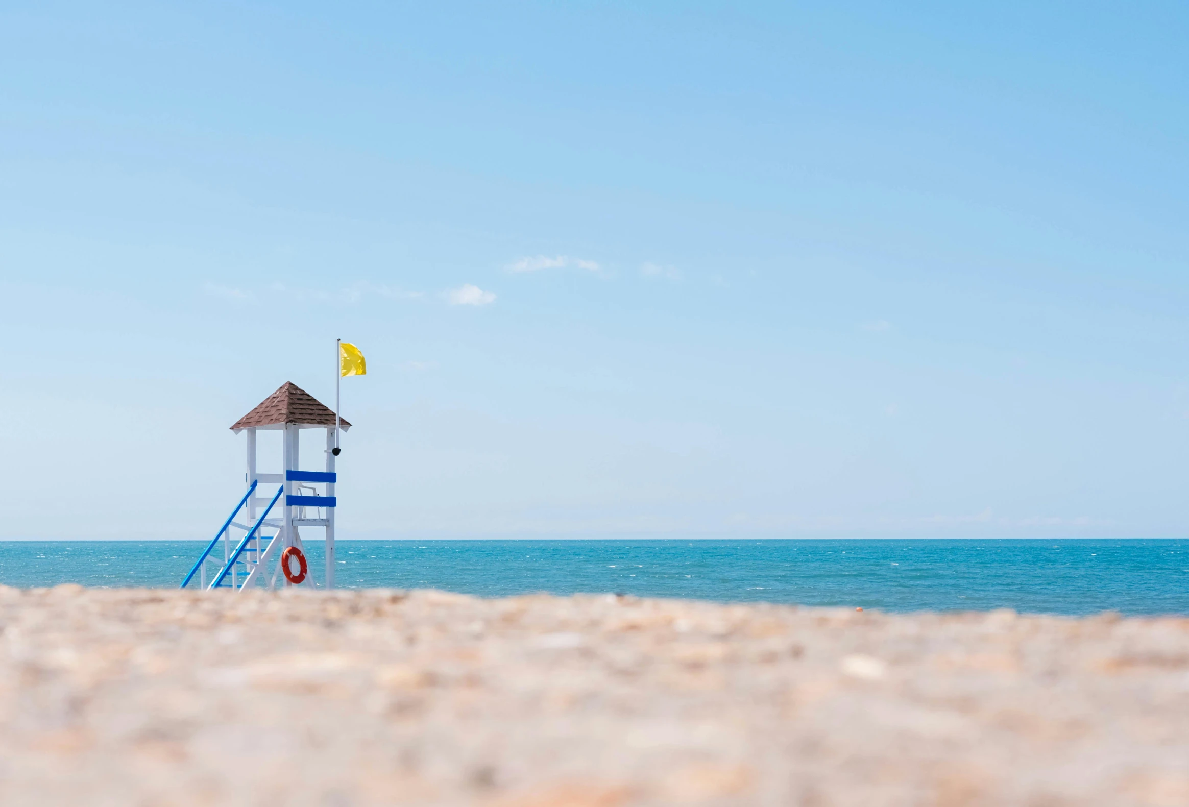 a lifeguard tower sitting on top of a sandy beach, unsplash, minimalism, clear blue skies, marbella landscape, shot on sony a 7, ultra shallow depth of field