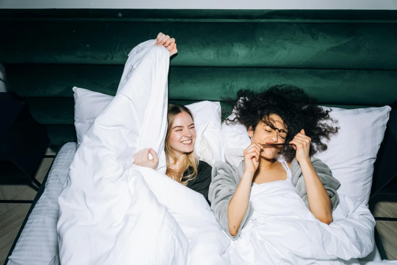 a couple of women laying on top of a bed, trending on pexels, silly, curled up under the covers, both laughing, julia hetta