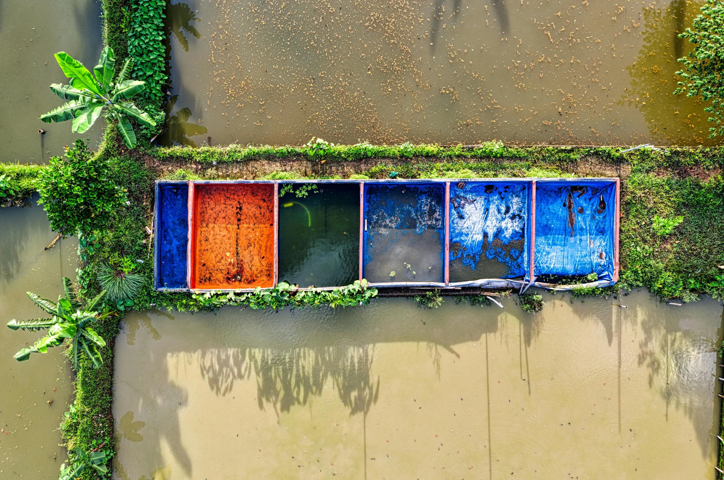 a river filled with lots of water next to a lush green forest, inspired by Steve McCurry, color field, boats in the water, orange and blue, jakarta, painted metal and glass