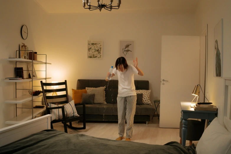 a woman standing in a living room next to a bed, by Adam Marczyński, pexels contest winner, happening, she is dancing. realistic, bounce lighting, wearing pajamas, low quality photo