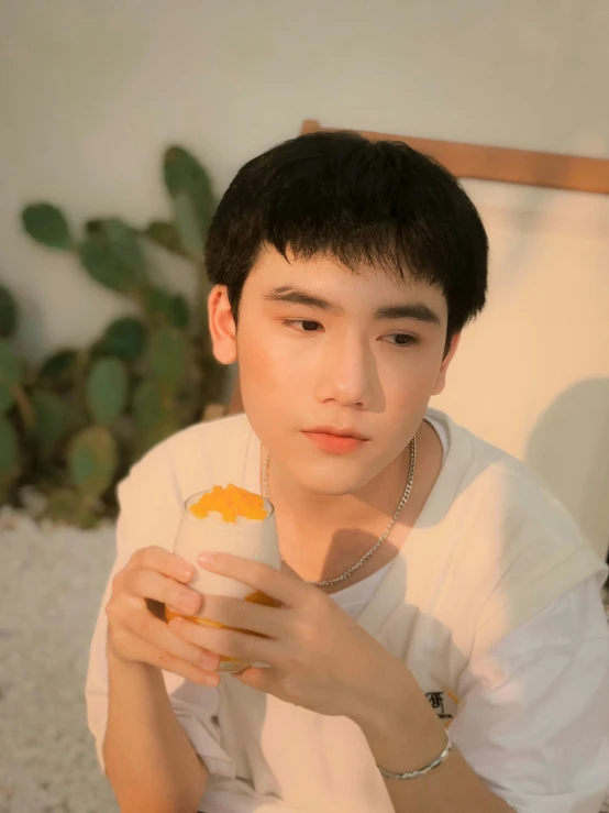 a man sitting on a bed holding a cup of coffee, an album cover, inspired by Bian Shoumin, trending on pexels, wan adorable korean face, holding a tangerine, profile image, soey milk