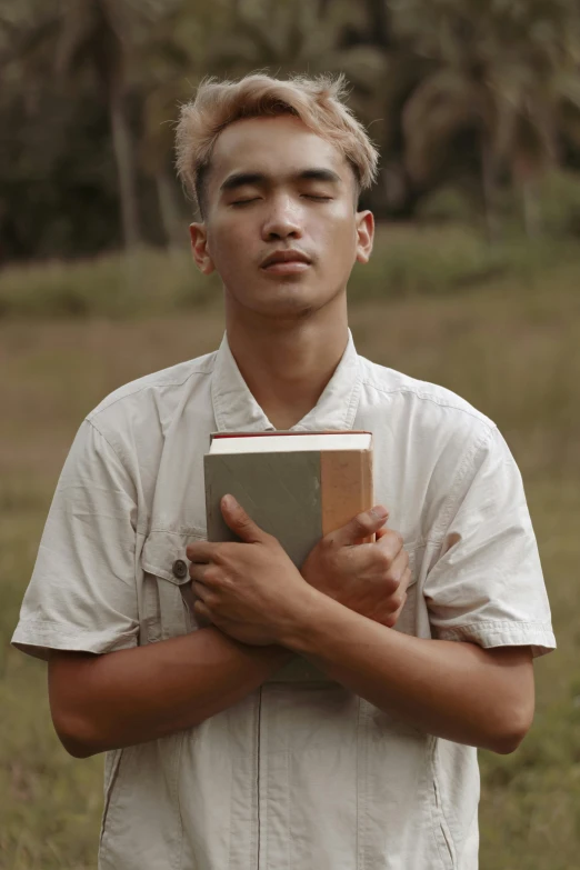 a man standing in a field holding a book, inspired by Nam Gye-u, unsplash, visual art, lean man with light tan skin, 18 years old, pray, with a bob cut