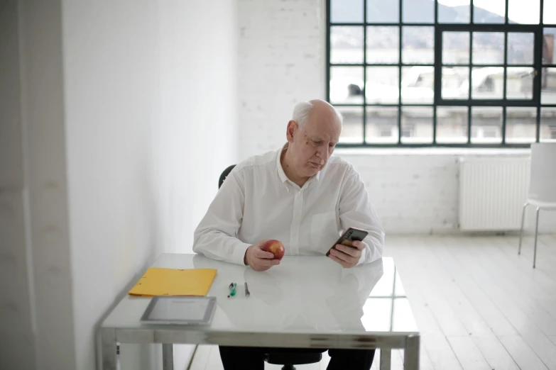 a man sitting at a table using a cell phone, inspired by Karl Ballmer, pexels contest winner, an apple, in white room, an oldman, in an call centre office