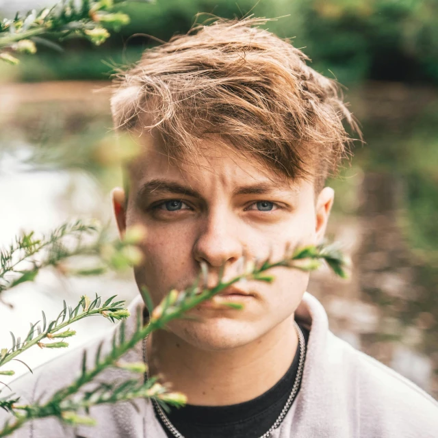 a man standing in front of a body of water, an album cover, inspired by Julian Allen, closeup headshot portrait, amongst foliage, caspar david, smug look