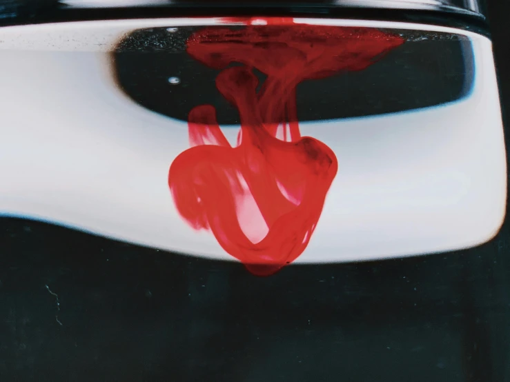 a glass filled with red liquid sitting on top of a counter, an album cover, inspired by Anish Kapoor, unsplash, process art, black oil bath, ignant, abstract claymation, 33mm photo