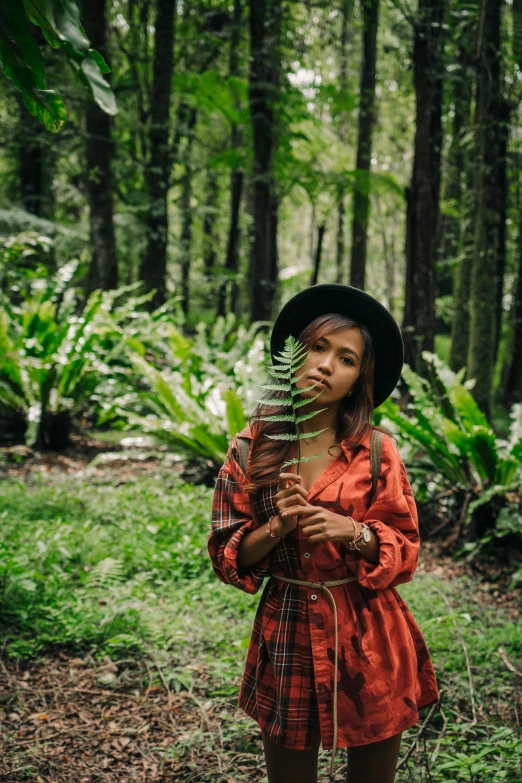 a woman standing in the middle of a forest, a portrait, pexels contest winner, sumatraism, avatar image, next to a plant, portrait of vanessa morgan, red dress and hat