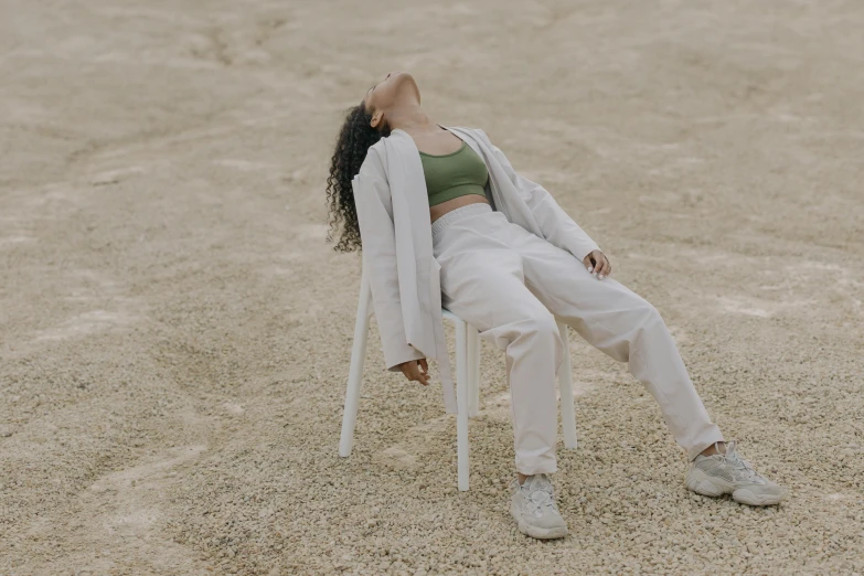 a woman sitting on a chair in the sand, trending on pexels, wearing a track suit, asleep, an all white human, an olive skinned