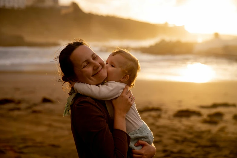 a woman holding a baby on a beach, by Matt Stewart, pexels contest winner, golden hour in pismo california, profile image, warm and joyful atmosphere, australian