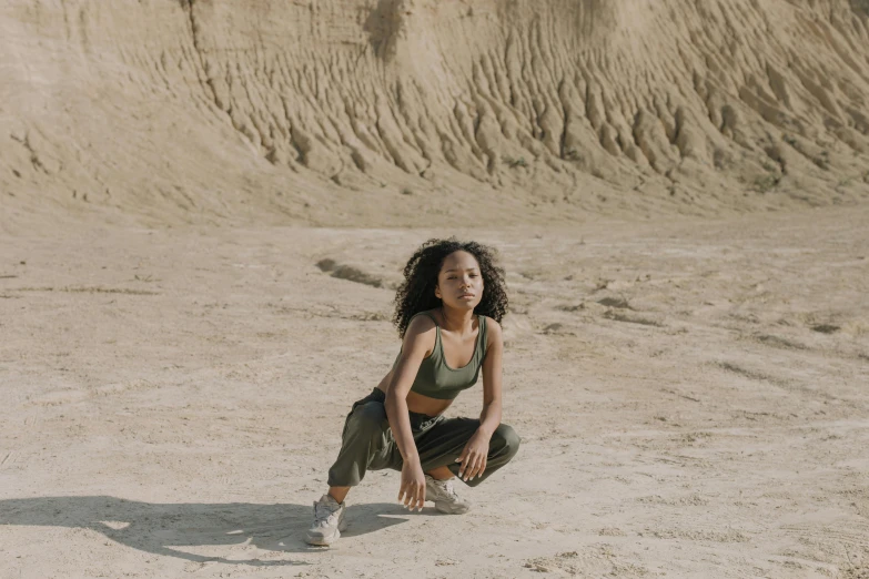 a woman crouches down to pick up a frisbee, an album cover, pexels contest winner, realism, rocky desert, portrait willow smith, sydney park, wearing adidas clothing