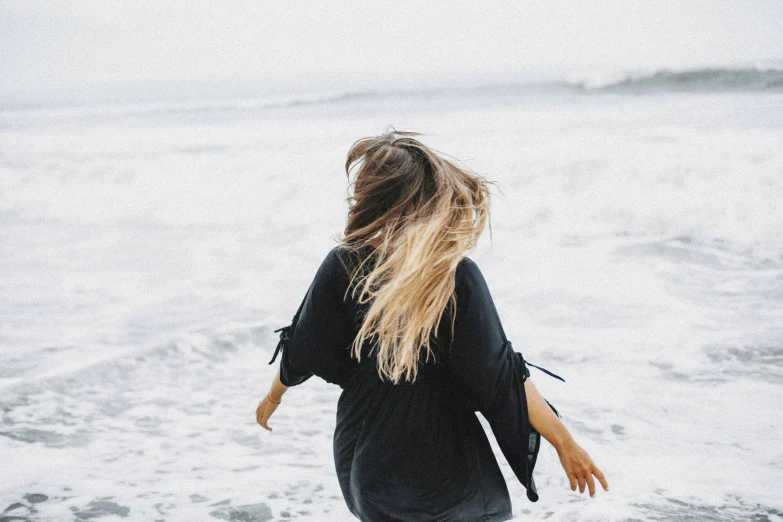 a woman standing on top of a beach next to the ocean, pexels contest winner, happening, tousled medium length hair, people running away, wearing black silk robe, instagram post