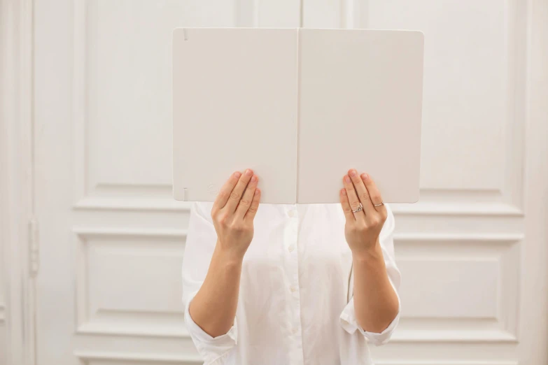 a woman covering her face with a book, an album cover, trending on unsplash, white finish, whiteboards, perfect symmetry, holding notebook