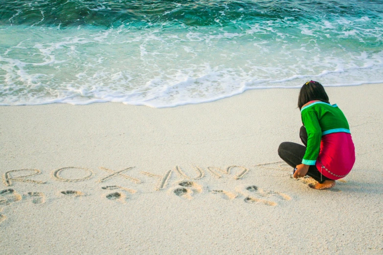 a person sitting on a beach writing in the sand, by Julia Pishtar, pexels contest winner, graffiti, okinawa japan, love os begin of all, a green, your name