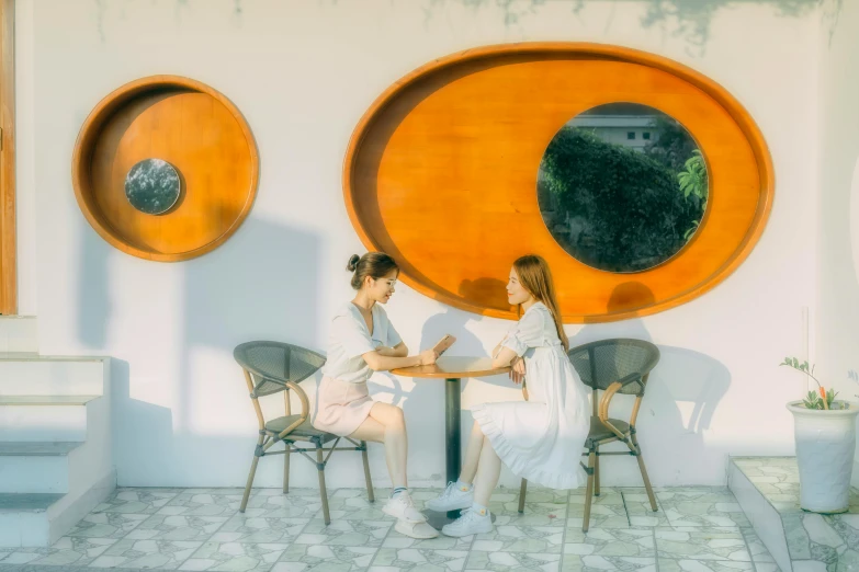 a couple of people that are sitting at a table, by Tan Ting-pho, pexels contest winner, realism, circle forms, summer day, white, two girls