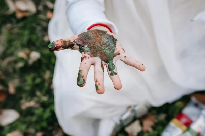 a close up of a person's hand with paint on it, a child's drawing, pexels contest winner, green and brown clothes, mud on face, sterile colours, gardening