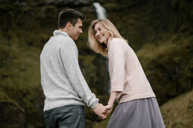 a man and woman holding hands in front of a waterfall, by Hallsteinn Sigurðsson, pexels contest winner, renaissance, flirting smiling, gray, cute woman, thumbnail