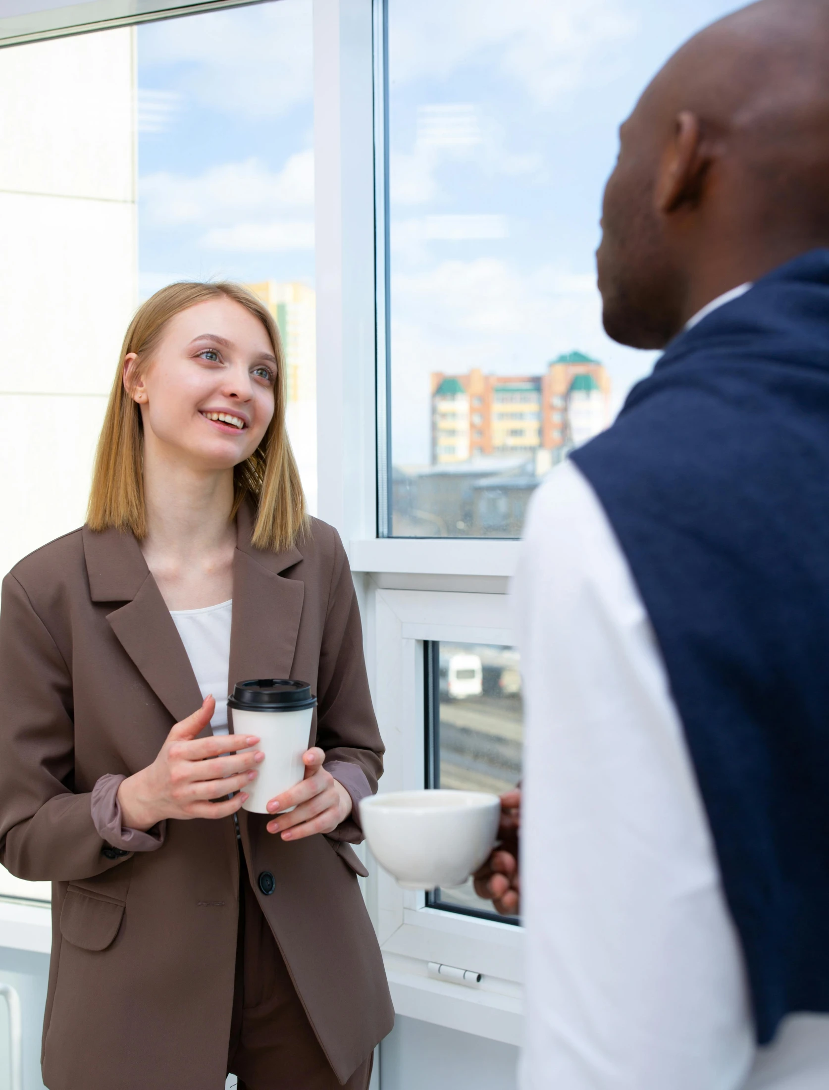 a woman standing next to a man holding a cup of coffee, happening, npc talking, girl in a suit, looking outside, lgbtq