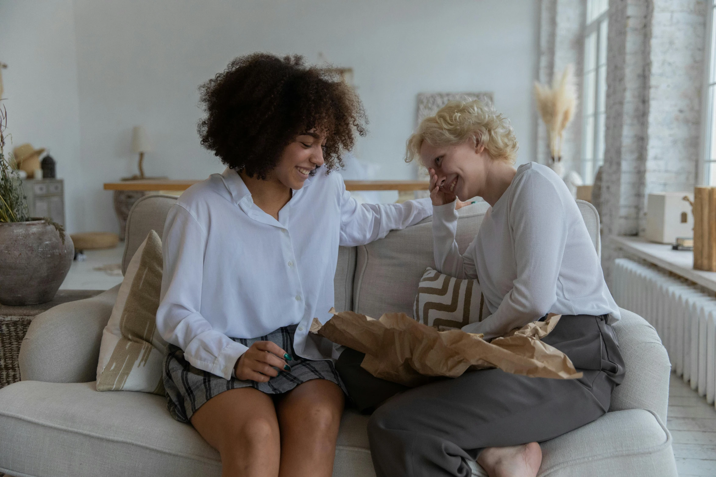 a couple of women sitting on top of a couch, pexels contest winner, earing a shirt laughing, short curly blonde haired girl, giving gifts to people, reuniting