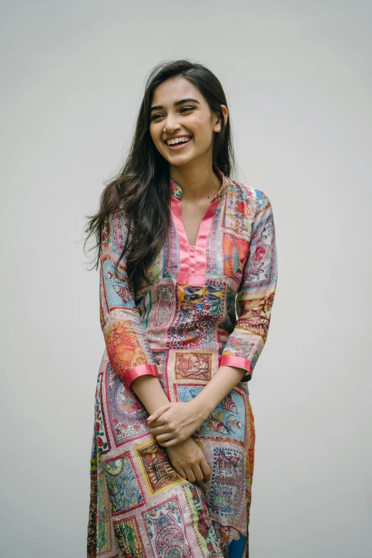 a woman standing in front of a white wall, pexels, hurufiyya, wearing a kurta, dua lipa, she is smiling, ad image