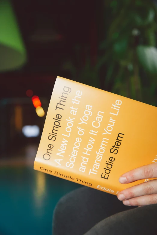 a close up of a person holding a book, an album cover, by Jessie Algie, trending on unsplash, on yellow paper, on a table, philosophy, sleek design