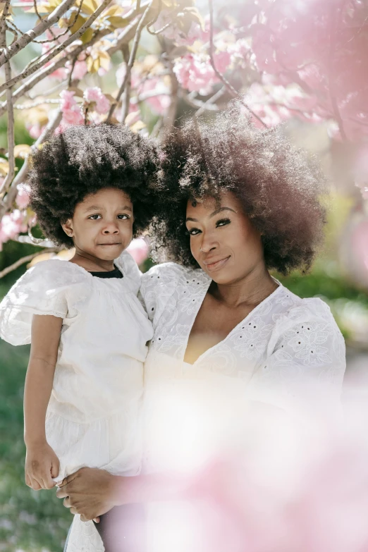 a woman holding a little girl under a tree, an album cover, pexels contest winner, afro hair, white blossoms, looking towards camera, instagram picture