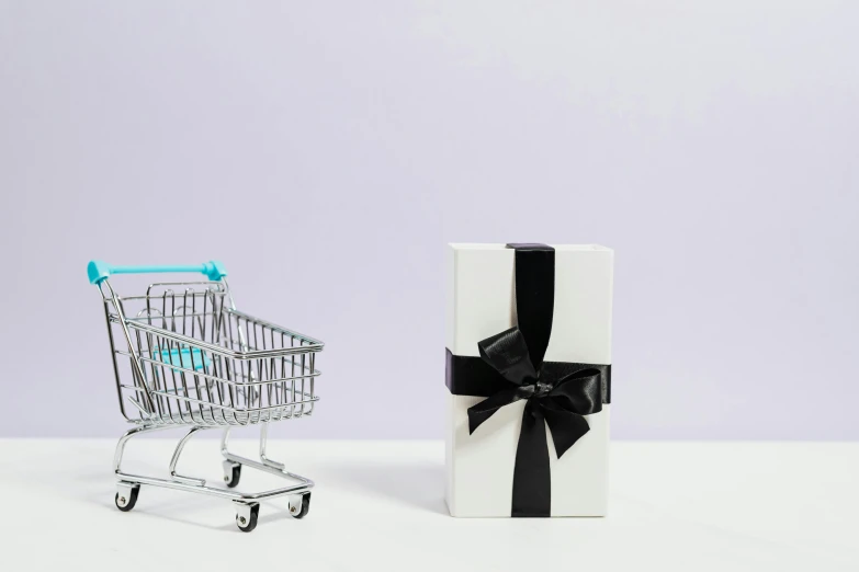 a shopping cart next to a gift wrapped in black ribbon, pexels contest winner, white box, arper's bazaar, pastel', facing sideways