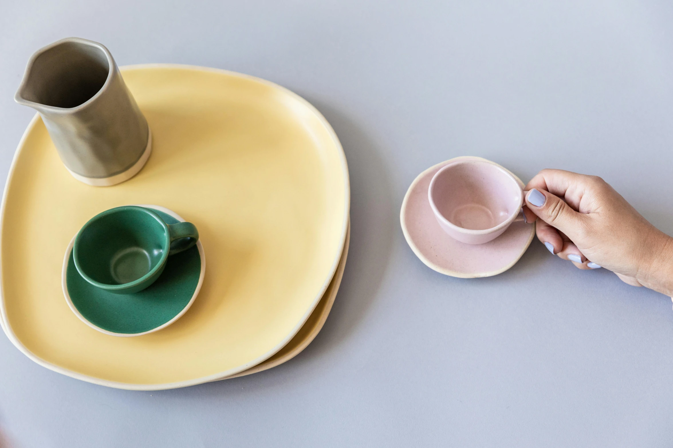 a person sitting at a table with a cup and saucer, a still life, inspired by Giorgio Morandi, trending on unsplash, minimalism, turquoise pink and yellow, made out of clay, square, various sizes