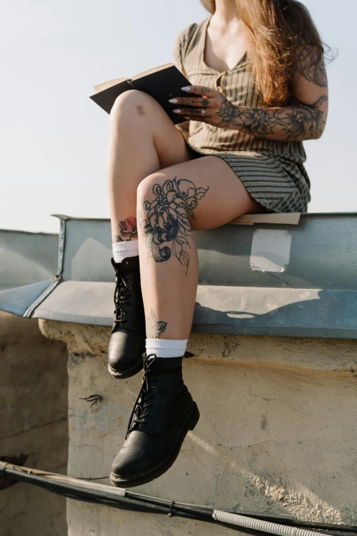 a woman sitting on a ledge reading a book, a tattoo, trending on pexels, hyperrealism, boots, rose tattoo, hot topic, rooftop