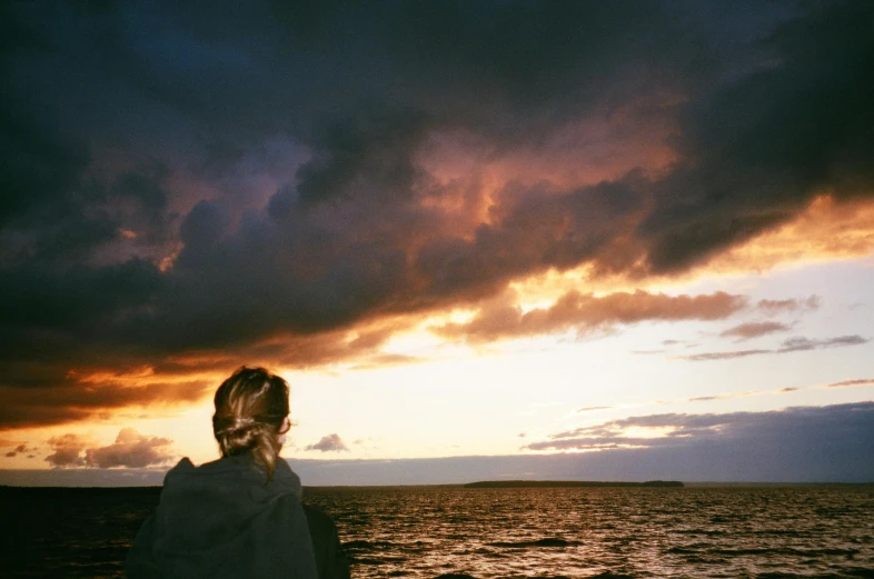 a woman looking out over the ocean at sunset, by Christen Dalsgaard, unsplash, storm clouds, on a boat, taken with kodak portra, greta thunberg