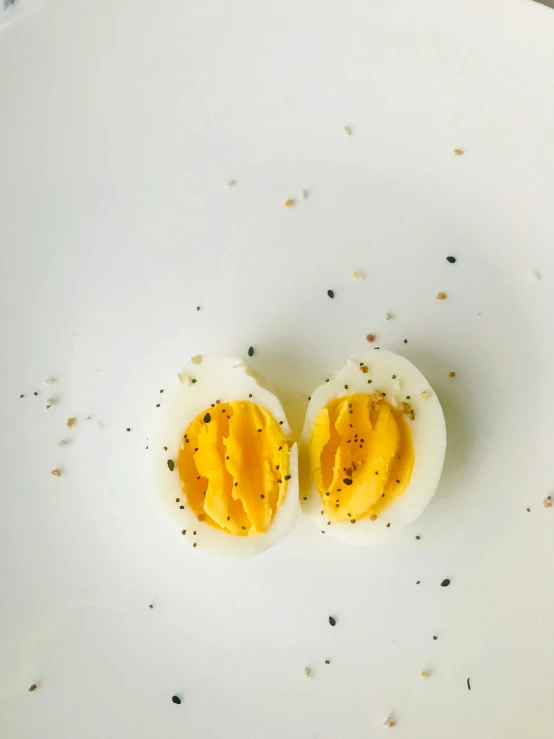 two halves of hard boiled eggs on a white plate, by Carey Morris, trending on pexels, pollen, petite, pepper, celebration