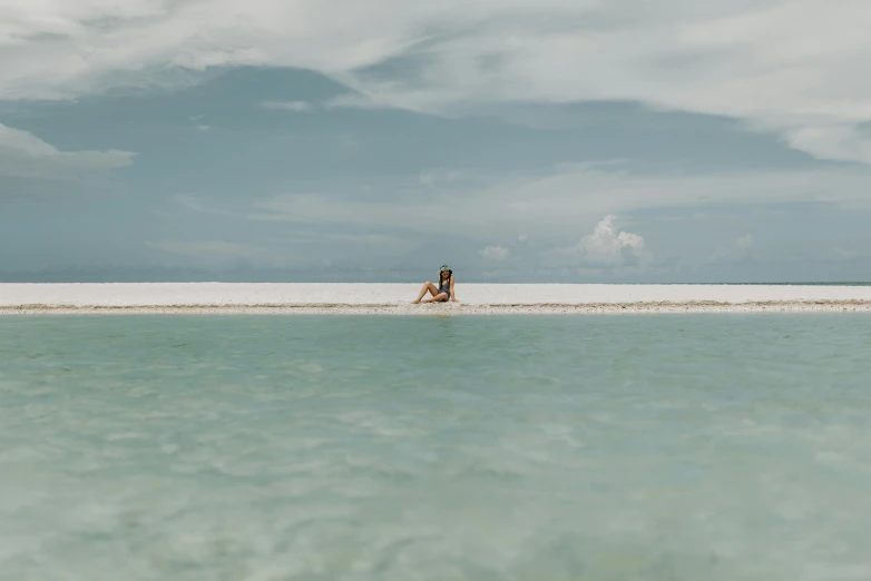 a person sitting on a beach next to a body of water, a picture, lagoon, medium format, floating into the sky, ben nicholas