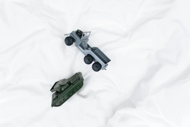 a couple of toy trucks sitting on top of a white sheet, unsplash, visual art, military weaponry, gray, lying in bed, enamel