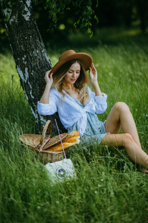 a woman sitting in the grass next to a tree, having a picnic, 5 0 0 px models, 2019 trending photo, straw hat