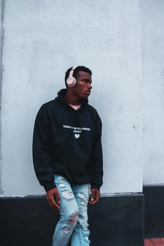 a man wearing headphones standing in front of a wall, inspired by Terrell James, trending on unsplash, hoodie, xxxtentacion, low quality photo, parental advisory