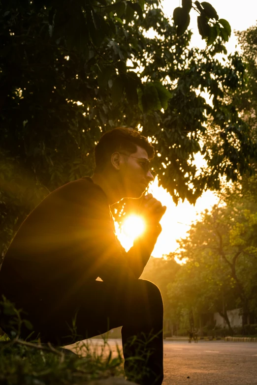 a man sitting on top of a skateboard next to a tree, by Rajesh Soni, pexels contest winner, romanticism, praying at the sun, backlit face, distant thoughtful look, profile pic