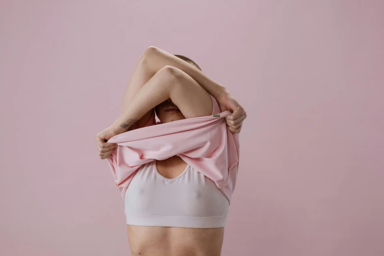 a woman holding a pink shirt over her head, trending on pexels, disrobed, silicone skin, made of lab tissue, wearing bra