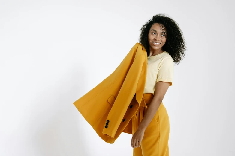 a woman standing with a yellow coat over her shoulders, trending on pexels, figuration libre, subject detail: wearing a suit, happy girl, with brown skin, detailed product image