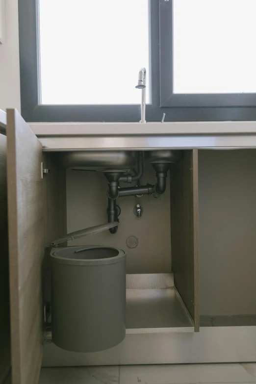 a white toilet sitting under a window next to a trash can, by Daarken, mechanical detail, dark kitchen, watertank, low pressure system