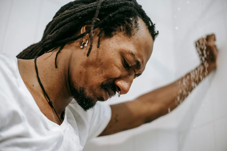 a man with dreadlocks standing in front of a shower, trending on pexels, process art, kara walker, man in white t - shirt, background image, filling with water