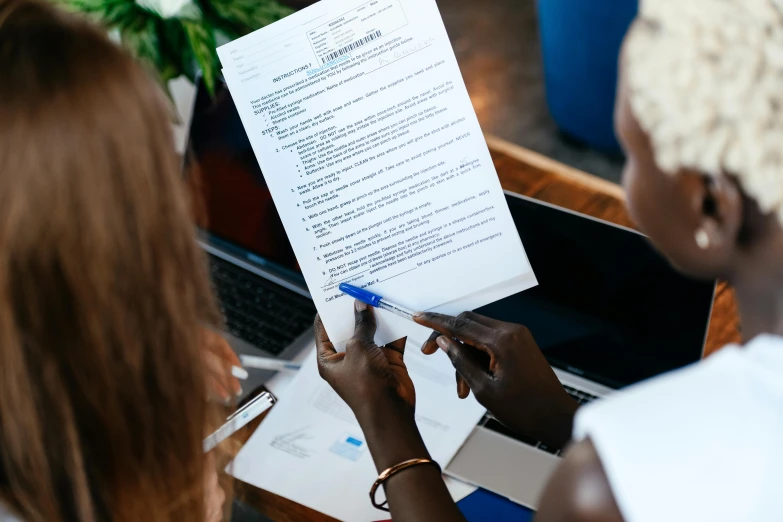 two women sitting at a table with papers in front of them, pexels contest winner, holding a clipboard, avatar image, back towards camera, closeup - view