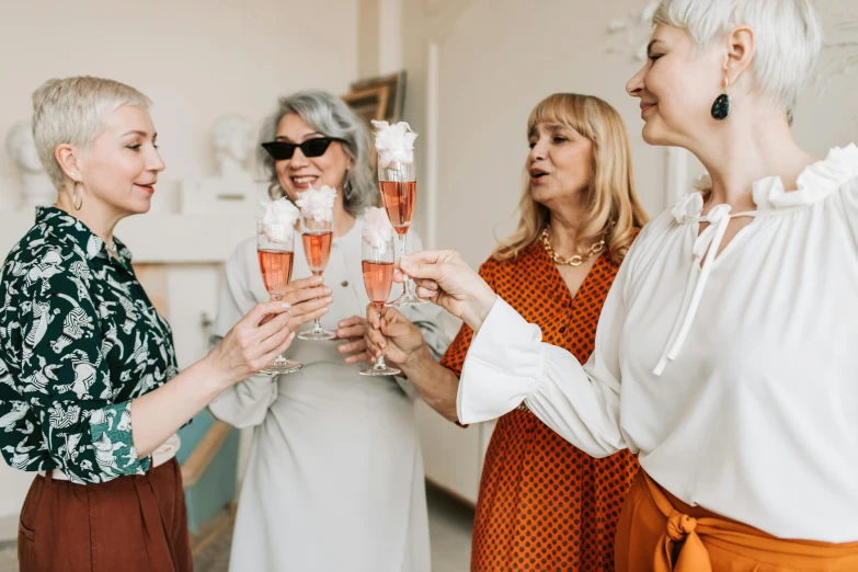 a group of women standing next to each other holding wine glasses, by Emma Andijewska, pexels contest winner, art nouveau, white and pink cloth, middle - age, wearing orange sunglasses, champagne commercial