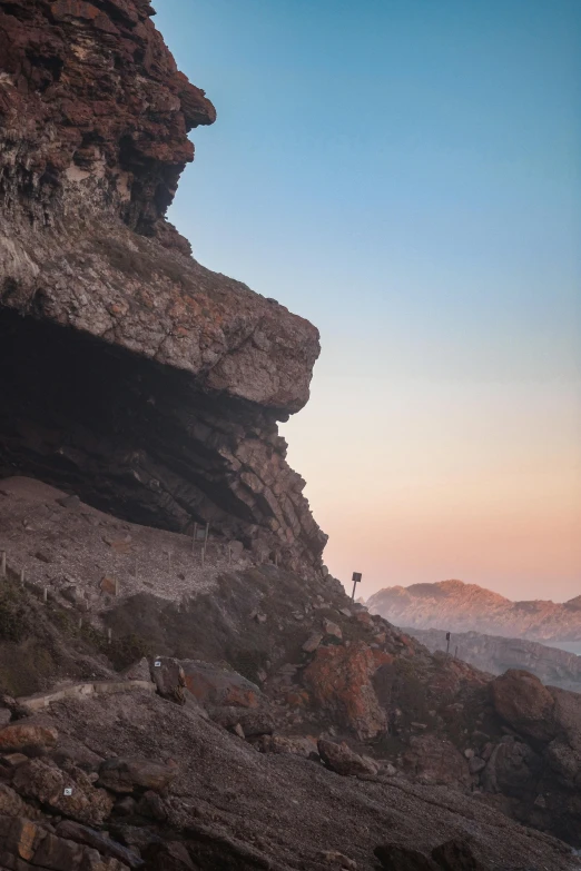 a man standing on top of a mountain next to a cave, les nabis, in a sunset haze, in socotra island, tiny people walking below, rock walls