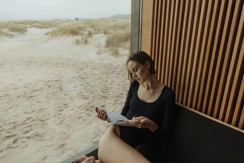 a woman sitting on a bench reading a book, by Emma Andijewska, happening, black swimsuit, sauna, in a beachfront environment, black