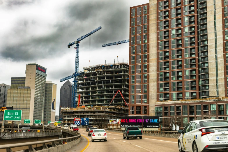 a group of cars driving down a highway next to tall buildings, by Dan Frazier, pexels contest winner, construction site, hyper - detailed color photo, building facing, clayton crain