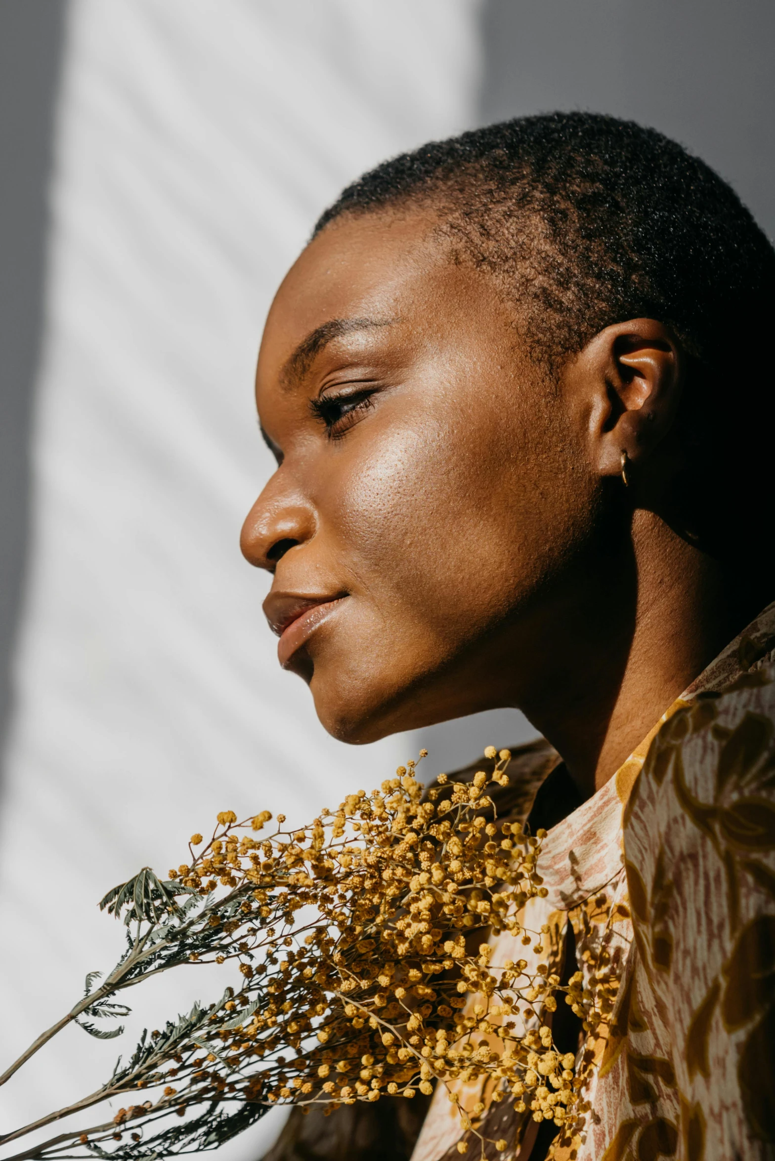 a woman holding a bunch of flowers in her hand, trending on unsplash, visual art, brown skin. light makeup, profile portrait of a woman, gold dappled light, sharp cheekbones