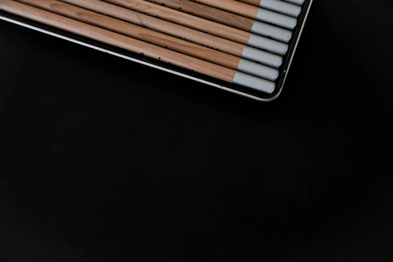 a bunch of pencils sitting on top of a table, inspired by Colin McCahon, unsplash, minimalism, smoker, square lines, metal lid, with a black background