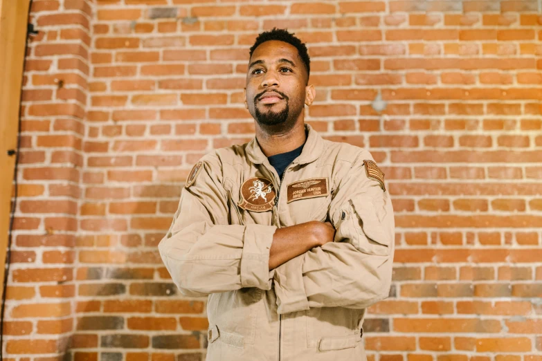 a man standing in front of a brick wall, flight suit, aaron brooks, official store photo, profile image