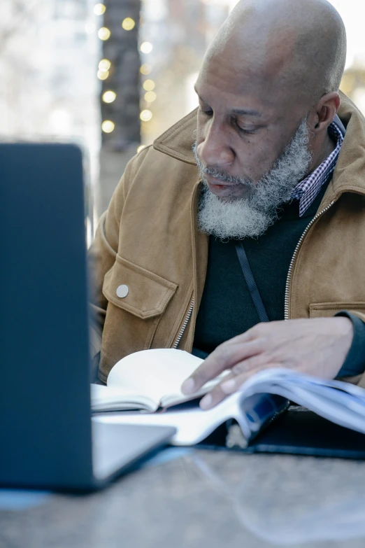 a man sitting in front of a laptop computer, by Robert Medley, pexels contest winner, renaissance, bald head and white beard, black man, reading engineering book, winter