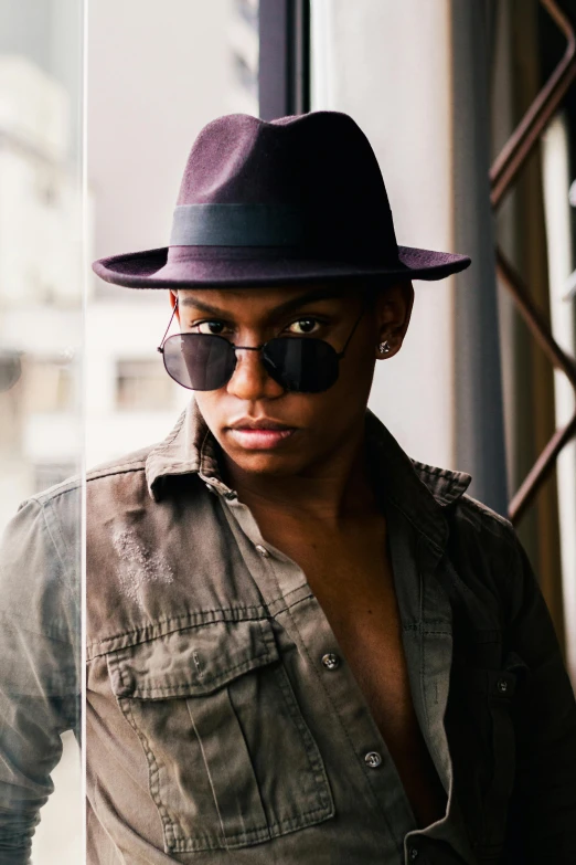 a man wearing a hat and sunglasses standing in front of a window, inspired by Byron Galvez, trending on pexels, beautiful androgynous prince, qiyana, in sao paulo, lights